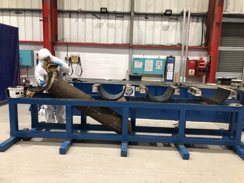 Technician in white PPE working on a steel clamp assembly component at a workstation in LJF Custom Coatings facility