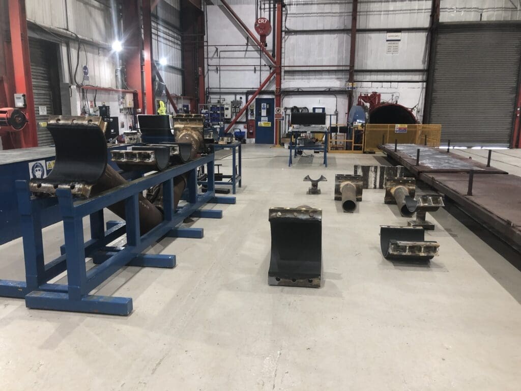 Multiple steel clamp and half-shell pipeline components laid out across workstations at LJF Custom Coatings facility
