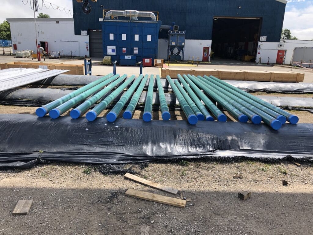 Fusion Bonded Epoxy (FBE) coated pipes with blue end caps stored outdoors at LJF Custom Coatings facility