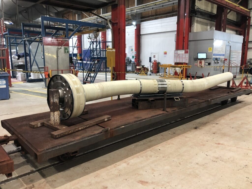 Curved flanged spool coated in white EPDM and PU thermal insulation staged on steel platform at LJF Custom Coatings facility