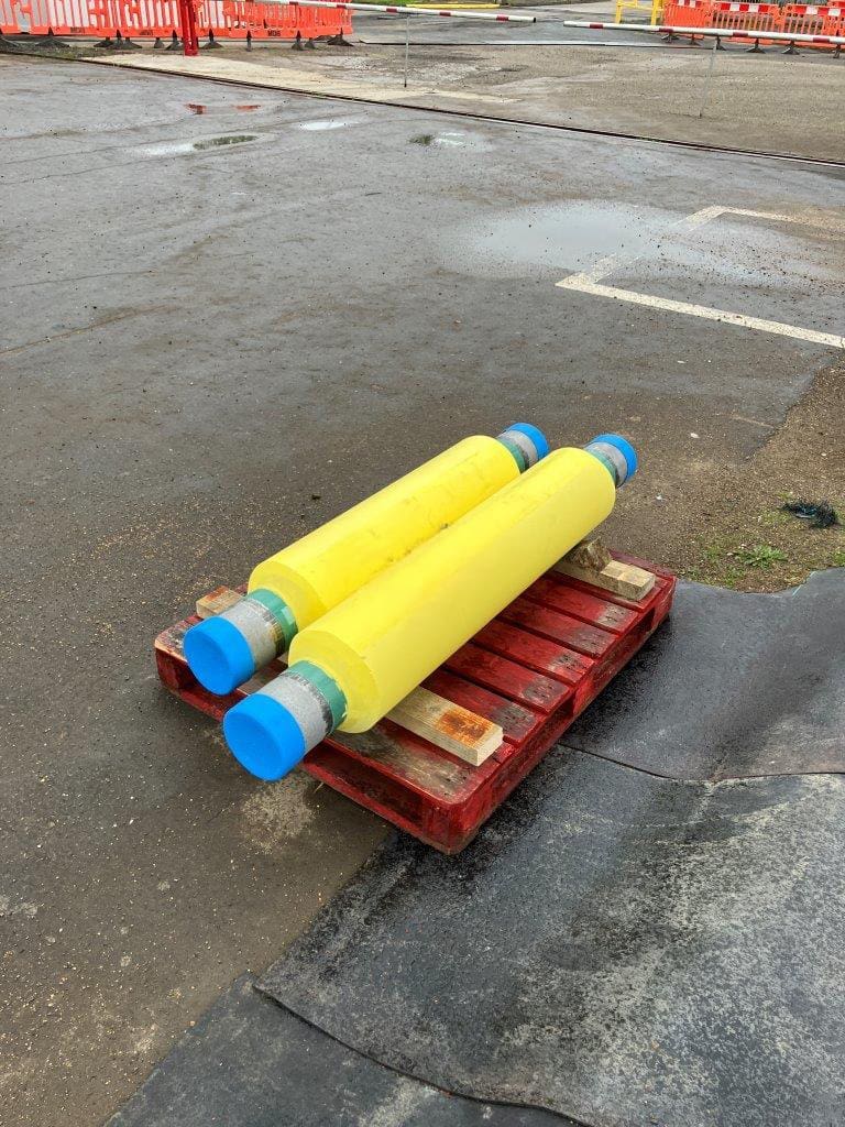 Two yellow PU-insulated pipe spools with blue end caps on a red pallet, ready for transport at LJF Custom Coatings facility